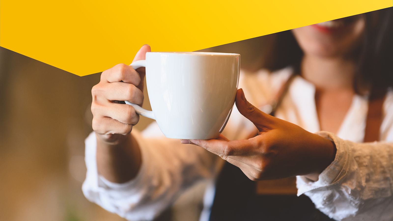 Une femme tient une tasse de café devant la caméra (avec un élément de design jaune par-dessus)