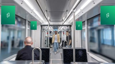 Vista interna di un mezzo pubblico con diverse superfici pubblicitarie all’interno della carrozza; sullo sfondo si vedono passeggeri sfocati.