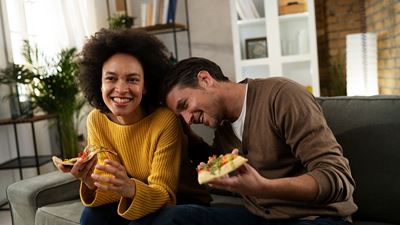 Due persone mangiano insieme la pizza sul divano